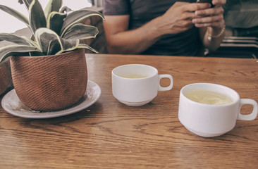Conceptual photo showing two cups of tea and a person using the phone to show the effects of technology, social media and the internet in everyday life and relationship 
