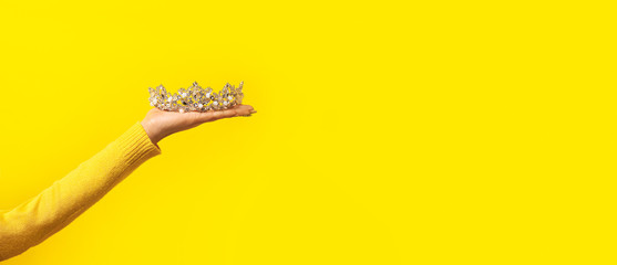 Shining diadem on female hand over yellow background, panoramic mock-up with space for text