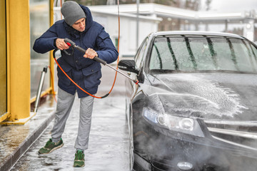 Shot of a man washing his car under high pressure water outdoors.