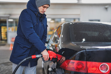 Close-up of a man pumping gasoline into a car at a gas station.