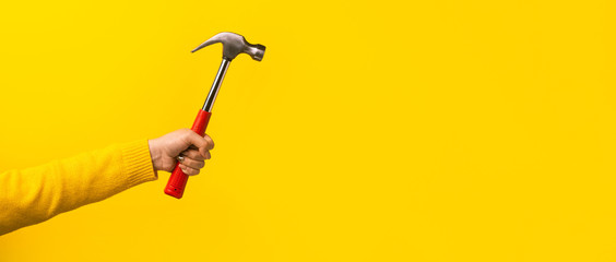 Female hand holding hammer on yellow background, panoramic mock-up