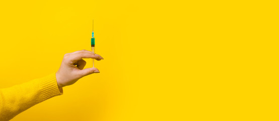hand holding syringe with medicine over yellow background, panoramic mock-up with space for text