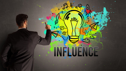 businessman drawing colorful light bulb with INFLUENCE inscription on textured concrete wall, new...