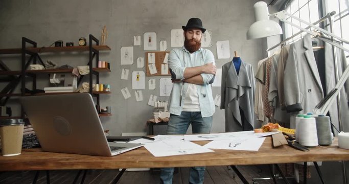 Bearded hipster fashion designer is wandering around his office, looking for inspiration for new collection - fashion, small business concept 4k footage