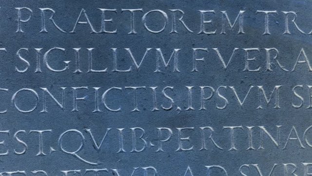 Blue color cast slow pan from right to left over old roman text letters words in Latin language carved in red stone