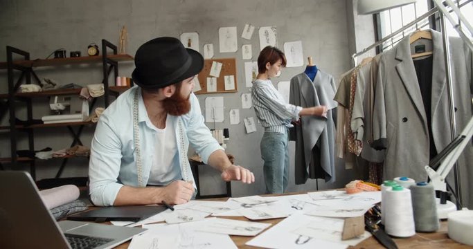 A hipster tailor couple is working together at their office, designing their new fashionable clothes collection - small family business concept 4k footage