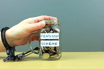 A hand holding and handcuffed to a jar of money. Locked into a pension scheme concept.