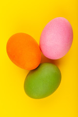 Colorful handmade Easter eggs. Top view of three eggs. Isolated on a yellow background. Preparing for Easter.