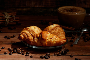Freshly baked French croissants with cappuccino milk on a dark background with copy space.