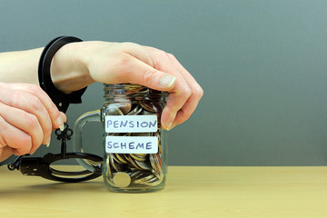 A hand holding a key to handcuffs attached to a glass jar of money. Locked into a pension scheme...