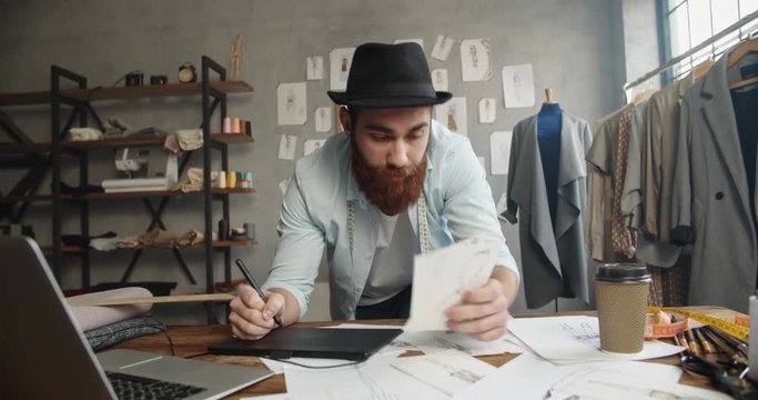 A male hipster clothing designer working in his office, redrawing his sketches to graphics tablet, making new collection - fashion concept 4k footage