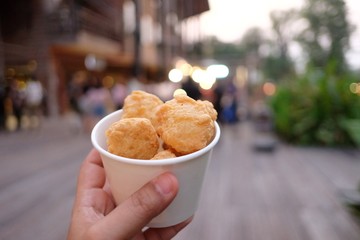 In selective focus of nuggets in a white paper box with a female hand holding and night market area