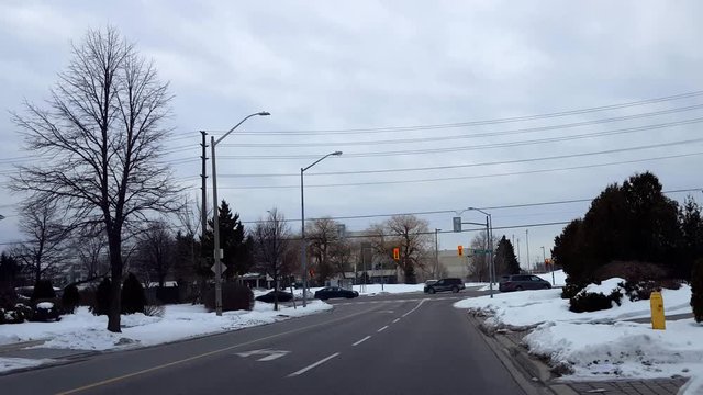 Cars Driving on Busy Street at City Light Intersection in Winter.  Vehicles Travelling on Urban Road With Moving Traffic and Snow.