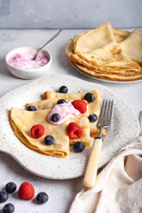 Russian pancakes with sour cream and berries, on a white plate on a white background. Maslenitsa week festival. Close-up vertical.