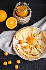 Russian cuisine, pancakes with orange jam and berries, on a plate on a dark wooden background. Maslenitsa week festival. Close-up vertical.