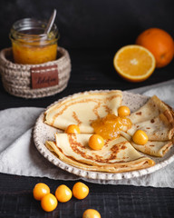 Russian cuisine, pancakes with orange jam and berries, on a plate on a dark wooden background. Maslenitsa week festival. Close-up vertical.
