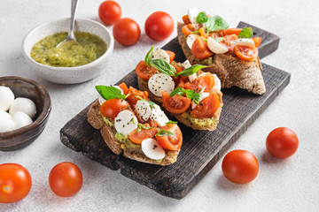 Italian snack bruschetta with tomatoes, mozzarella and basil on a dark wooden board on a white background, close up horizontal