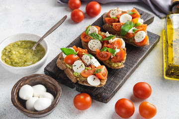 Italian snack bruschetta with tomatoes, mozzarella and basil on a dark wooden board on a white background, close up horizontal