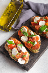 Italian snack bruschetta with tomatoes, mozzarella and basil on a dark wooden board on a white background, close up vertical
