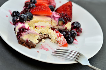 Close-up of half eaten cream strawberry, blueberry cheesecake tart on plate with spoon