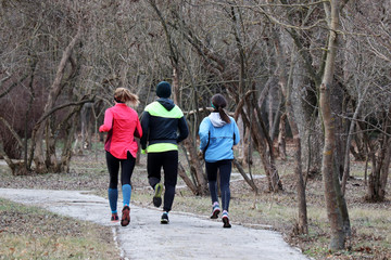 Guy and two girls running in a spring park, rear view. Concept of workout, people runners, slimming in cold season