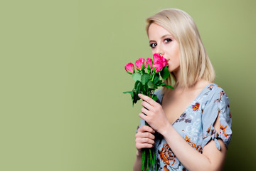 Beautiful blonde woman in dress with roses on green background
