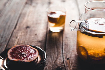 Citrus tea in a transparent teapot and a glass, healthy drink on a wooden background.