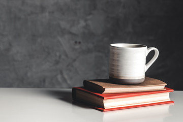 A cup of coffee on stack of books on grey background
