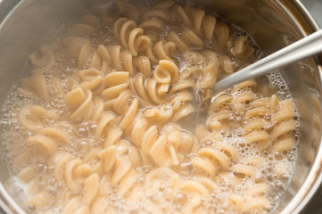 Whole grain pasta in a pan with boiling water and a spoon. Cooking healthy food.