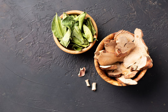 Dried galangal slice and kaffir lime leaves in a wooden bowls on a dark table. Top view. Copy space.