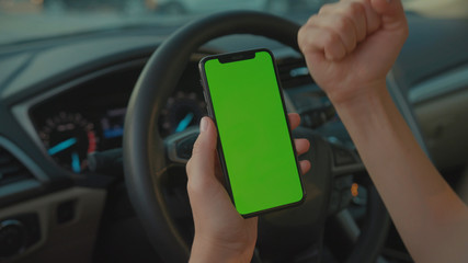 Lviv, Ukraine - May 19, 2018: Female driver sitting in the car browsing online map on vertical mock-up smartphone greenscreen searching route planning a roadtrip. Lifestyle and technology.
