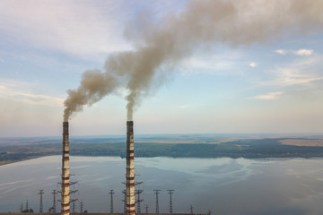 Naklejka na ściany i meble Aerial view of high chimney pipes with grey smoke from coal power plant. Production of electricity with fossil fuel.