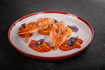 Boiled crayfish. Delicacy with chili pepper sauce, orange, zest, basil and capers on a plate. Gourmet cuisine. Dark concrete background