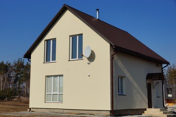 one large private gray house with white windows under a brown tiled roof stands in the dry grass against a blue sky on a sunny day