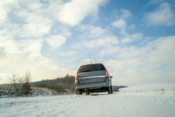 Family car driving on a dirt road in snow covered winter field.