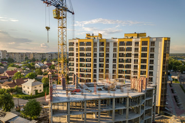 Apartment or office tall building under construction. Brick walls, glass windows, scaffolding and concrete support pillars. Tower crane on bright blue sky copy space background.