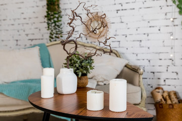 Fototapeta na wymiar white candles on wooden coffee table in cozy living room interior.Stylish scandinavian living room.Candle and plant in vase on small wooden table in front of scandinavian designed sofa. boho home