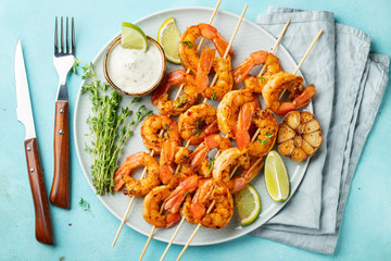 Grilled shrimp skewers or langoustines served with lime, garlic and sauce on a light blue concrete background. Seafood and beer. Top view. Flat lay