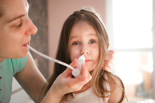 Mother using "Nose cleaner vacuum suction nasal mucus runny aspirator kids inhalation" to pull out the snot from nose. Little Girl has been sucking snot from running nose symptom by her mother.