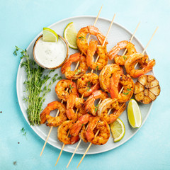 Grilled shrimp skewers or langoustines served with lime, garlic and sauce on a light blue concrete background. Seafood and beer. Top view. Flat lay
