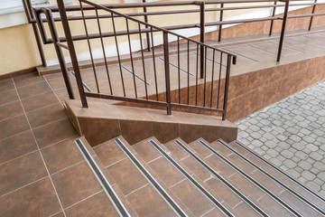 Concrete entrance stairs covered with ceramic tiles with metal railings outdoors.