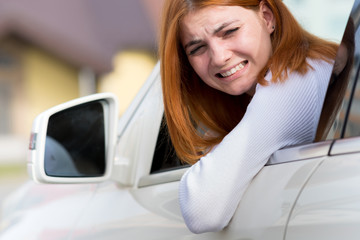 Young woman driving a car backwards. Girl with funny expression on her face while she made a fender...