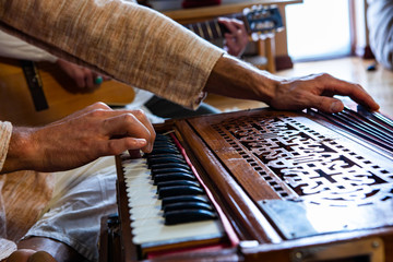Closeup of male shamanic hands playing sacred kirtan music with fingers on keys of harmonium while...