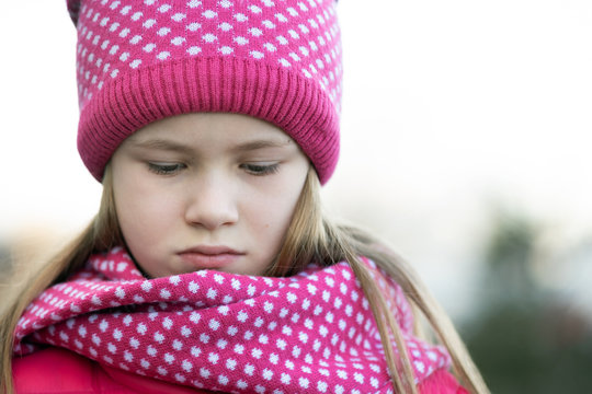 Sad child girl in warm knitted winter clothes outdoors.