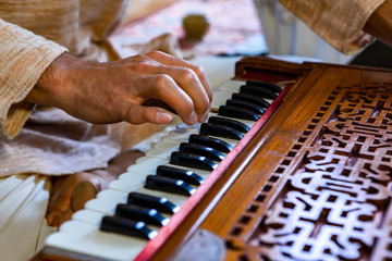Closeup of shamanic hands pressing harmonium keys playing sacred kirtan music for divine power and...