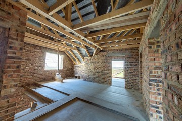 Attic of a building under construction with wooden beams of a roof structure and brick walls.