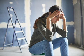 Portrait of frustrated young woman sitting on paint can devastated by renovations project, copy space