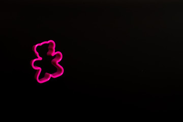 Pink plastic cookie cutter for making cookies in the shape of a teddy bear on a black background....