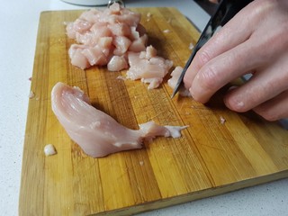 Male hand cuts with a knife slices of chicken meat, poultry fillet