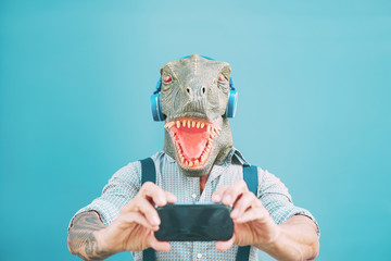 Senior fashion man taking selfie with mobile smartphone while wearing t-rex mask - Hipster guy...